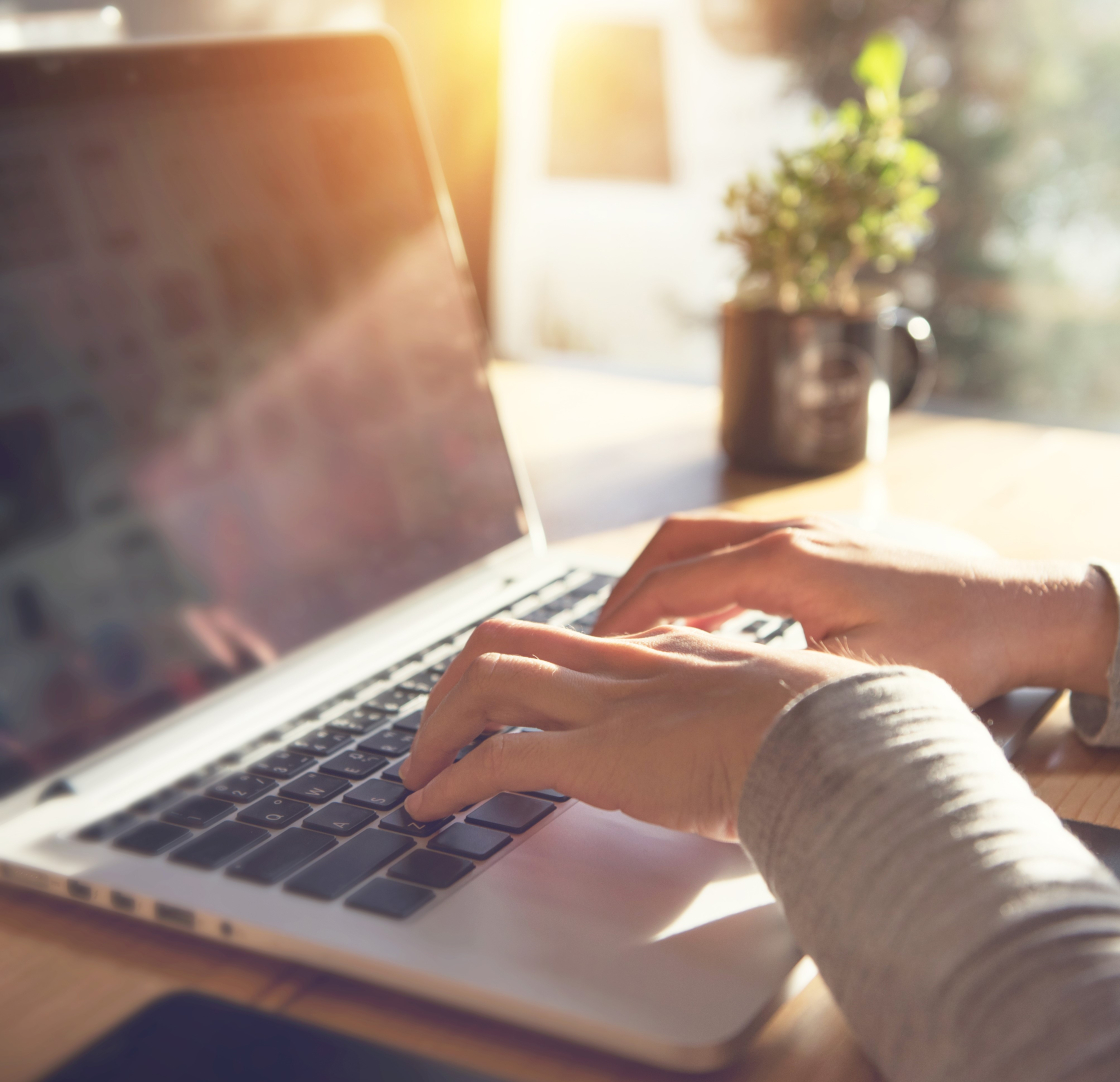 A woman types on a laptop. Sunlight streams in through her window.